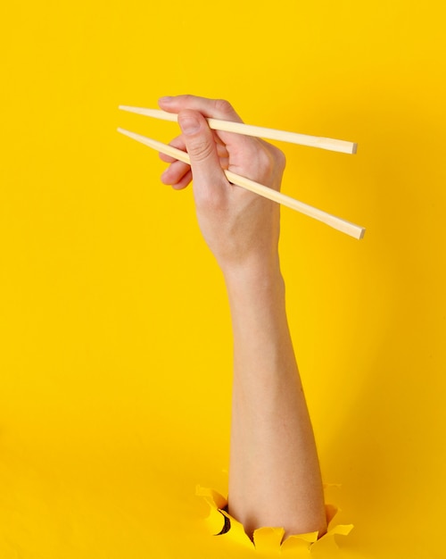 Femme main tenir les baguettes à travers le trou déchiré sur jaune. Concept alimentaire minimaliste. Vue de dessus