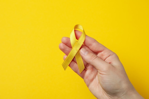 Femme main tenir le ruban de sensibilisation au cancer de l'enfant sur jaune