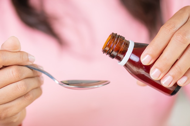 Femme main verser un sirop antipyrétique de la bouteille à la cuillère. concept de soins de santé.