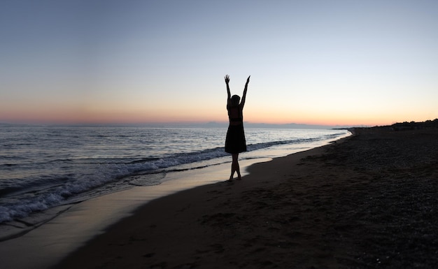 Photo femme avec les mains en l'air sur la plage au coucher du soleil