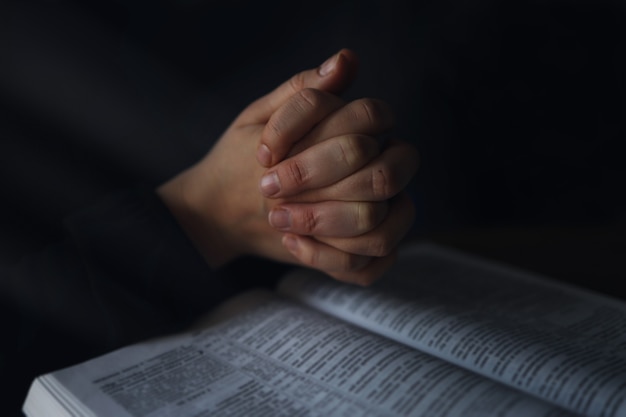 Femme les mains sur la Bible. elle lit et prie sur la bible dans un espace sombre au-dessus d'une table en bois.