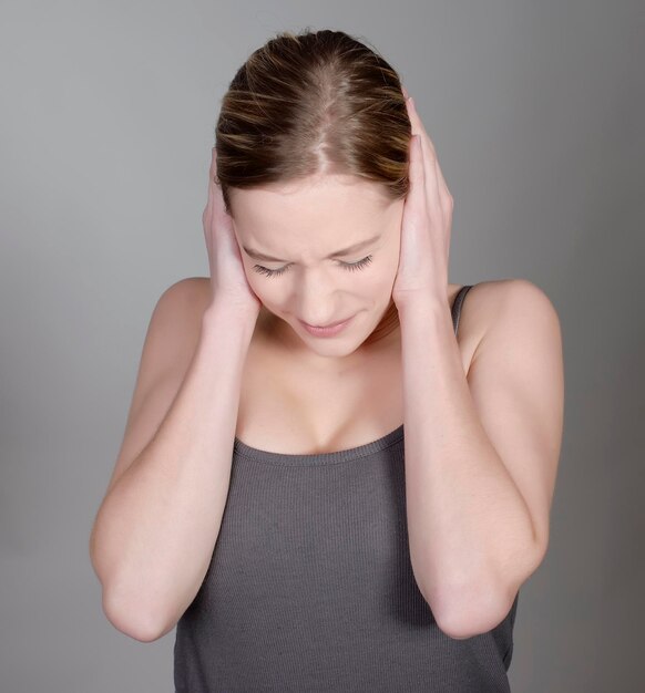 Femme avec les mains couvrant les oreilles sur un fond gris