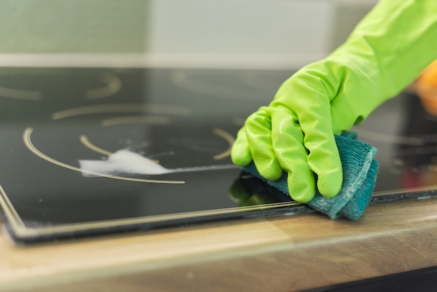 Femme mains dans les gants nettoie la plaque vitrocéramique électrique de cuisine avec une éponge et un détergent