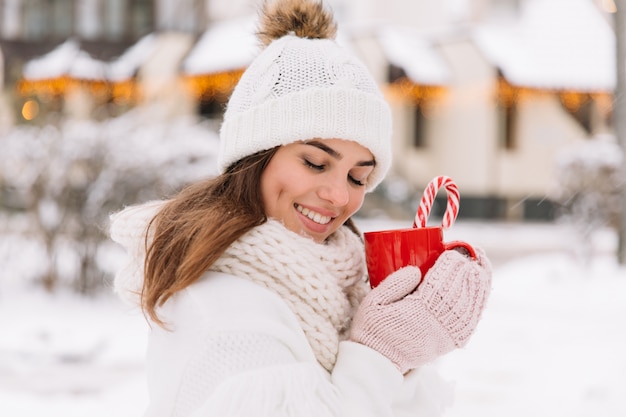 Femme mains dans les gants tenant une tasse confortable avec du cacao chaud, du thé ou du café et une canne en bonbon.