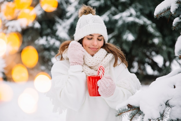 Femme mains dans les gants tenant une tasse confortable avec du cacao chaud, du thé ou du café et une canne en bonbon.