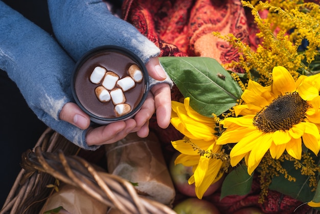 Une femme les mains dans des mitaines tenant une tasse de chocolat chaud ou de cacao