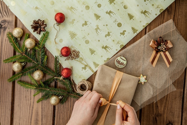 Femme, mains, emballage, cadeau noël, gros plan Noël non préparé présente sur bois avec des éléments de décoration et des éléments, vue de dessus. Emballage de bricolage de Noël ou du nouvel an.