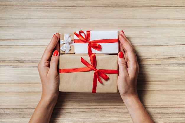 Femme mains tenant des coffrets cadeaux de Noël décorés de rubans de satin sur une surface en bois