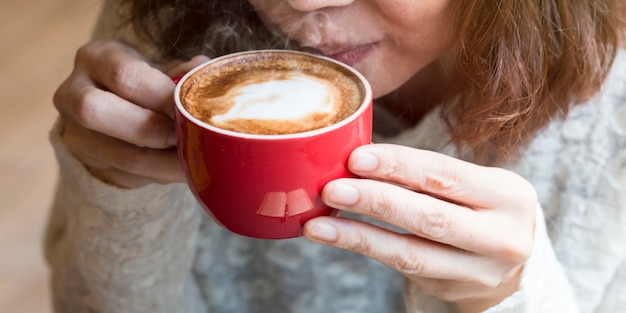 Femme des mains tenant une tasse de café au lait près de la fenêtre