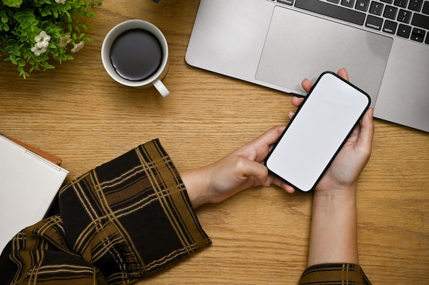 Une femme mains tenant ou utilisant son smartphone à sa vue de dessus de bureau en bois minimal