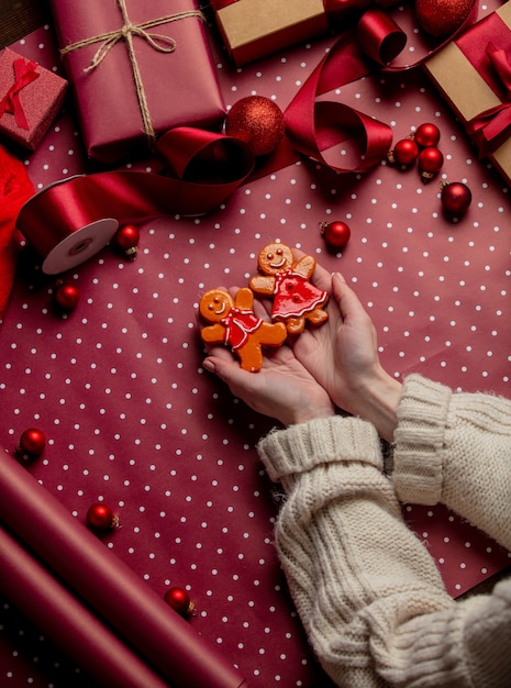 Femme mains tenir biscuit homme en pain d'épice près de cadeaux sur papier d'emballage