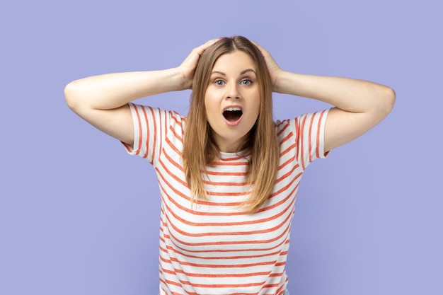 Femme avec les mains sur la tête exprimant son étonnement en gardant la bouche largement ouverte