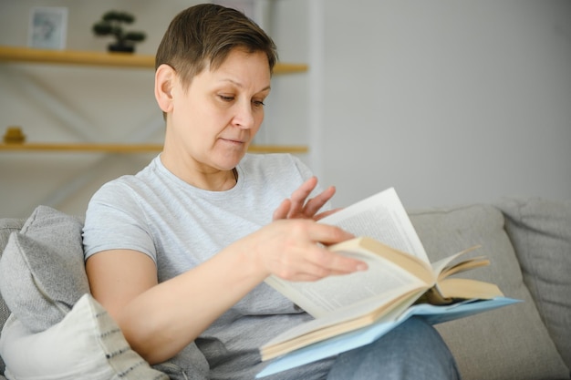 Femme à la maison assise sur un canapé lisant un livre