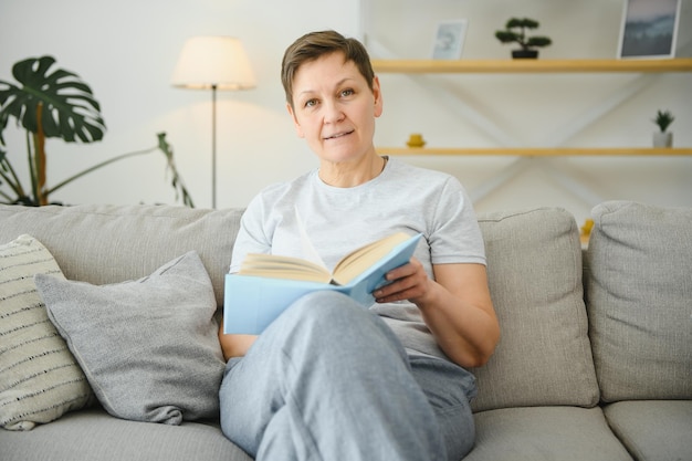 Femme à la maison assise sur un canapé lisant un livre