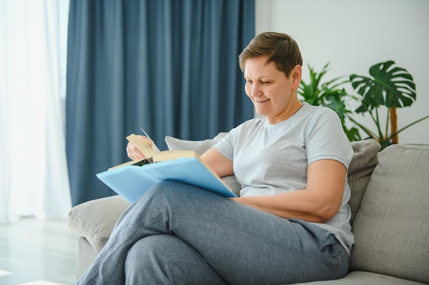 Femme à la maison assise sur un canapé lisant un livre