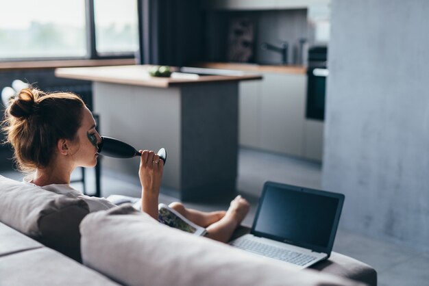 Femme à la maison en chemise de nuit avec un magazine, un verre et des patchs sur son visage.