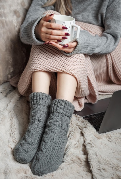 Une femme à la maison confortable recouverte d'une couverture chaude boit du café