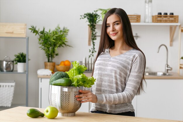 Femme sur la maison de la cuisine avec la cuisson des légumes verts. Vitamines de régime alimentaire à domicile Helthy jeune et belle femme. Prise de vue en studio.