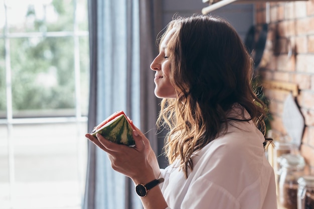 Femme à la maison mangeant de la pastèque dans la cuisine