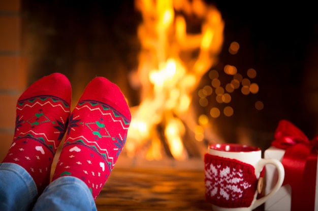 Femme à la maison. Pieds dans des chaussettes de Noël près de la cheminée. Détente et confort. Concept de vacances d'hiver