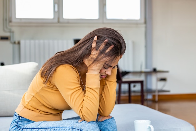 Femme avec un mal de tête assis sur le canapé