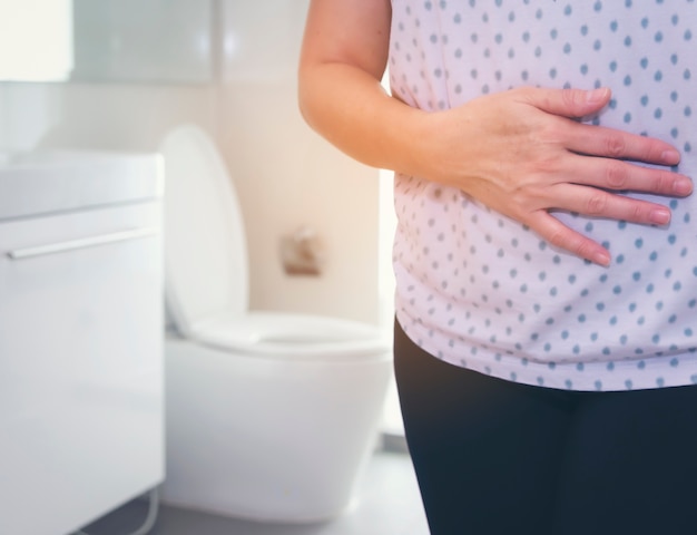 Une femme a un mal de ventre devant les toilettes.