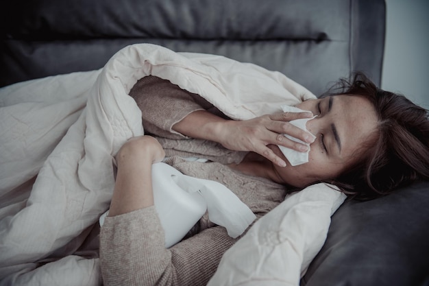 Une femme malade asiatique s'assoit sur le canapé reste à la maison La femme se sentait mal voulait s'allonger et se reposerforte fièvre