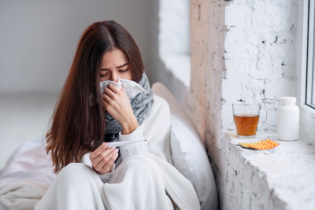 Femme malade attrapée froide, se sentant malade et éternuant dans une lingette en papier