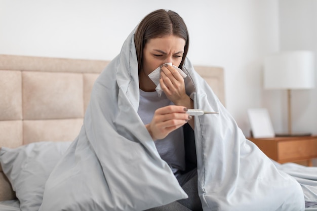 Photo une femme malade au lit qui vérifie sa température avec un thermomètre se sent mal.