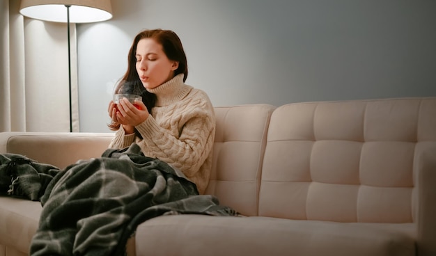 Femme malade de la grippe avec une tasse de thé chaud contre la toux soufflant sur lui