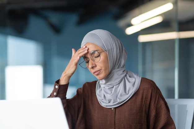 Femme malade en hijab travaillant à l'intérieur d'un immeuble de bureaux moderne