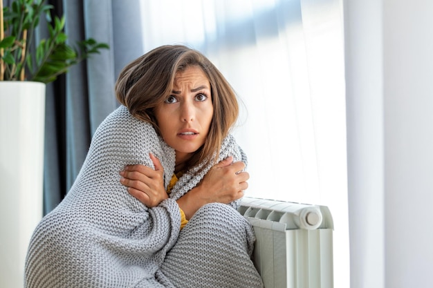 Photo une femme malade locataire dans une couverture s'assoit dans un salon froid main sur un vieux radiateur souffre du manque de chaleur une jeune femme malsaine lutte contre le gel froid à la maison pas de concept de chauffage