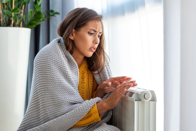 Une femme malade locataire dans une couverture s'assoit dans un salon froid main sur un vieux radiateur souffre du manque de chaleur Une jeune femme malsaine lutte contre le gel froid à la maison Pas de concept de chauffage