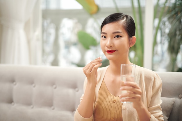 Femme malade mangeant des pilules avec un verre d'eau à la main.