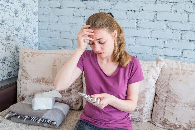 Une Femme Malade Avec Un Rhume Regarde Les Pilules. Fièvre élevée Et Maux De Tête Dus à La Grippe Et Aux Maladies Virales. Traitement à Domicile. Volgodonsk, Russie 04 Mai 2019