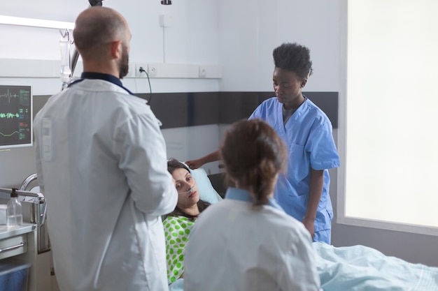 Femme malade se reposant dans son lit avec tube à oxygène nasal lors d'un rendez-vous médical à l'hôpital. Médecins praticien surveillant le patient examinant le symptôme de la maladie tout en écrivant un traitement de récupération