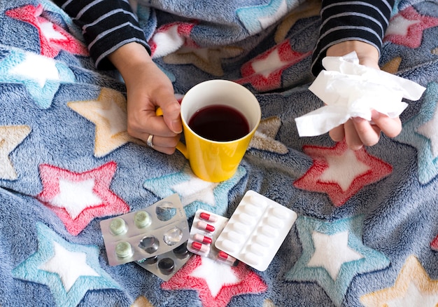 Photo femme malade sous la couverture, buvant du thé et prenant des pilules