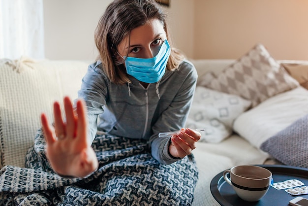 Une femme malade vérifie le thermomètre ayant de la fièvre Une fille porte un masque de protection ayant la grippe froide à la maison montre un panneau d'arrêt