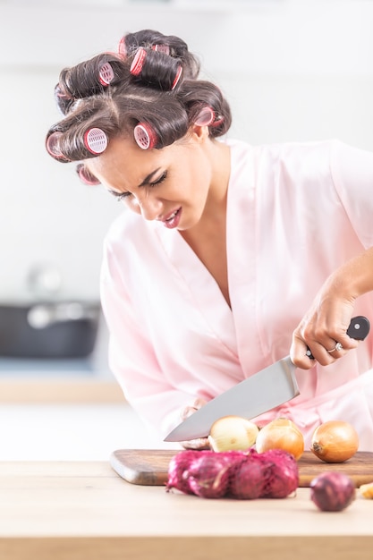 Photo une femme malheureuse avec des bigoudis coupe l'oignon avec un couteau.