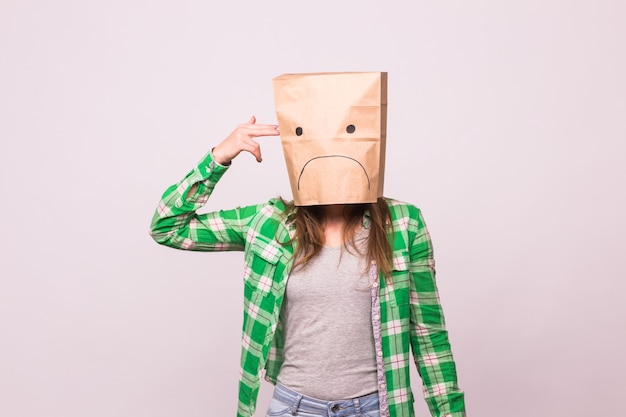 Femme malheureuse avec une émoticône triste devant un sac en papier sur la tête sur fond blanc