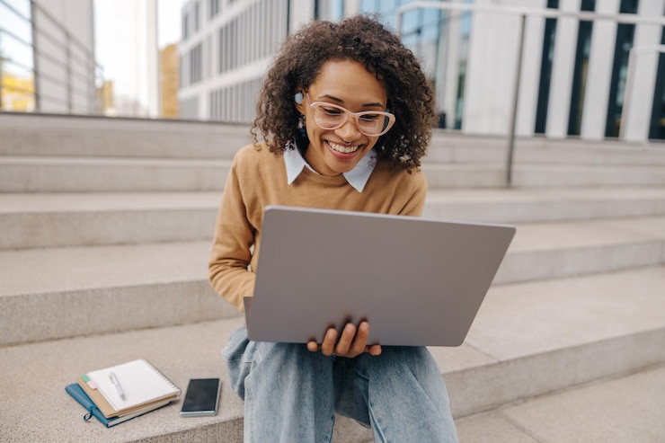 Photo une femme manager souriante avec des lunettes travaille sur un ordinateur portable assise sur l'arrière-plan d'un immeuble de bureaux