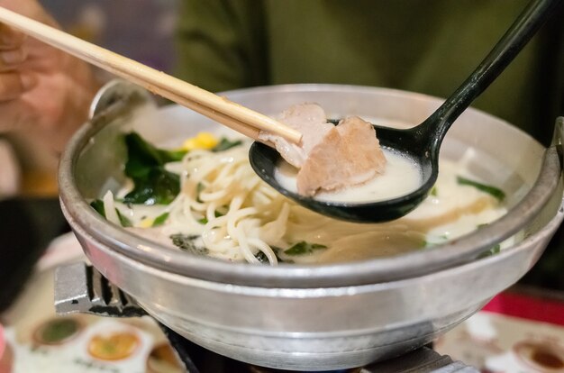 Une femme mange un bol de ramen tonkotsu au restaurant