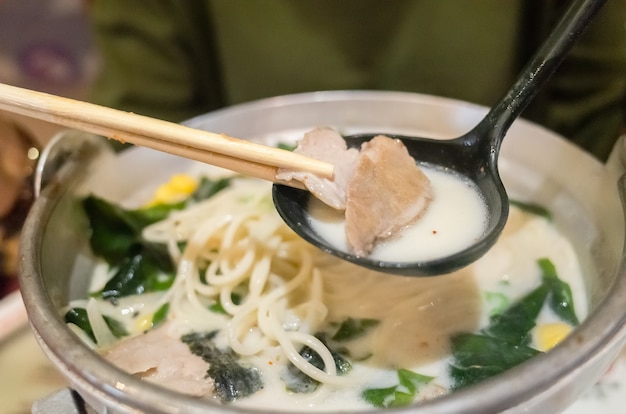 Une femme mange un bol de ramen tonkotsu au restaurant