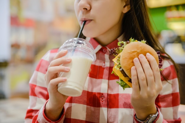 Une femme mange un humburger et boit un milk-shake en gros plan