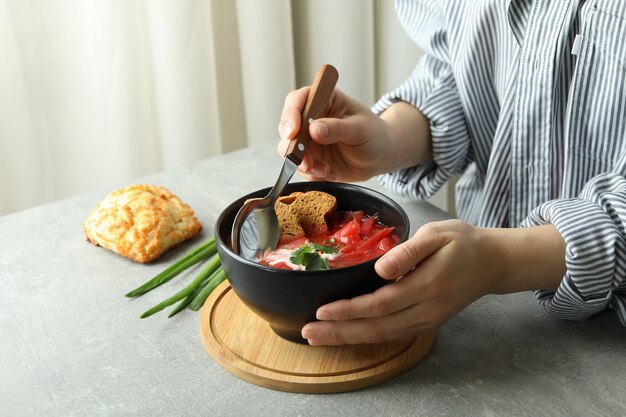 Femme mange savoureux bortsch sur table grise avec du pain et de l'oignon