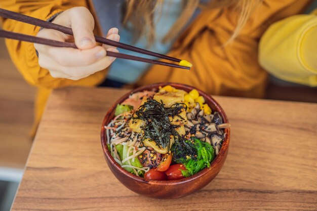 Femme mangeant un bol de poke bio cru avec du riz et des légumes gros plan sur la table vue de dessus