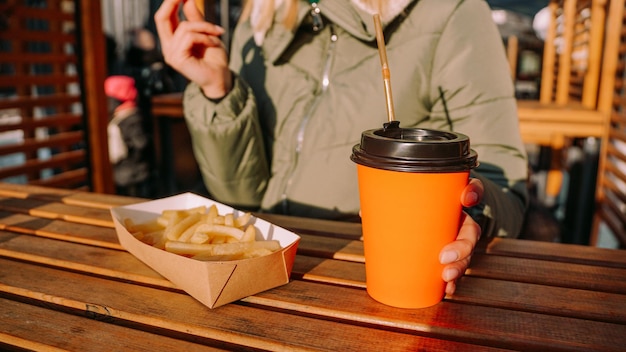 Femme mangeant de délicieuses frites et buvant du thé ou du café dans un café en plein air