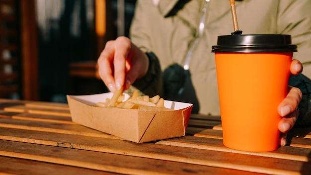 Femme mangeant de délicieuses frites et buvant du thé ou du café dans un café en plein air