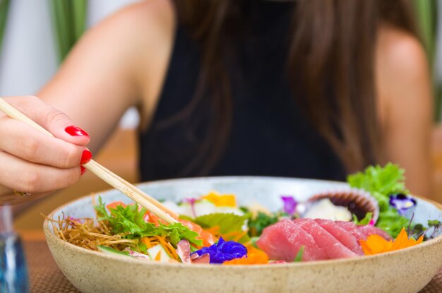 Femme mangeant de délicieux sashimi gros plan sur des baguettes