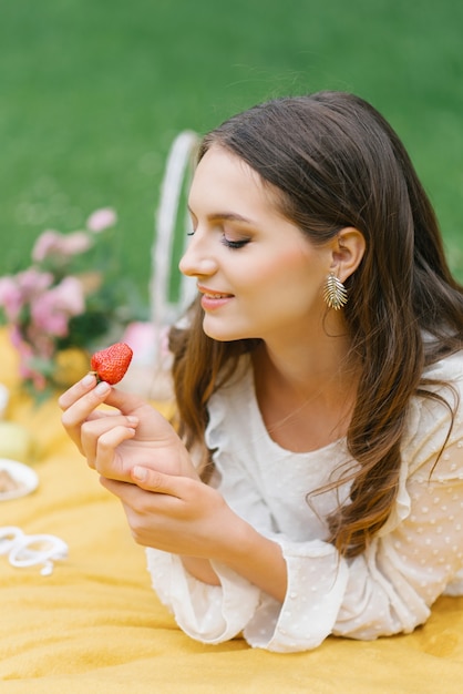 Une femme mangeant des fraises lors d'un pique-nique d'été, un charmant sourire. Portrait en gros plan.